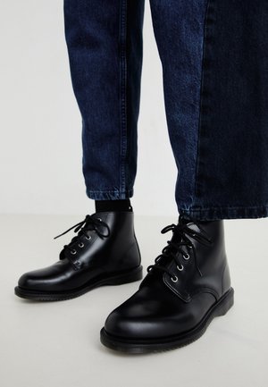 Black leather ankle boots with round toes, lace-up design, and metal eyelets. Worn with dark blue denim pants, featuring a straight-cut shape.