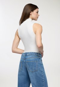 Top aderente bianco senza maniche con collo alto abbinato a jeans leggeri azzurri a vita alta, caratterizzati da una vestibilità comoda e tasche posteriori classiche.