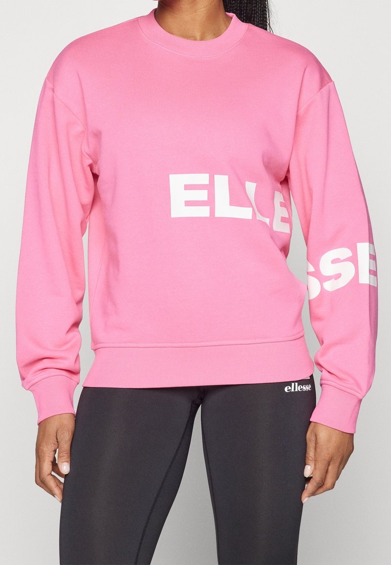 Sweat-shirt rose à manches longues et col rond. Présente le texte blanc "ELLESSE" sur le devant et la manche. À assortir avec des leggings noirs.