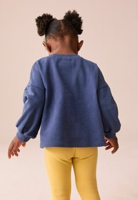 Niebieski sweter z bufiastymi rękawami, ściągaczami i zaokrąglonym dekoltem, zestawiony z żółtymi legginsami. Miękka tekstura i swobodny fason.