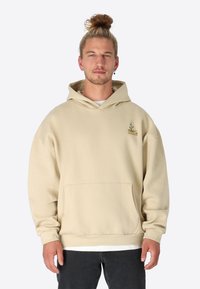 Beige Kapuzenpullover mit großer Fronttasche, Kordelzugkapuze und grünen gestickten Details. Weicher Stoff mit lässiger Passform und gerippten Bündchen.
