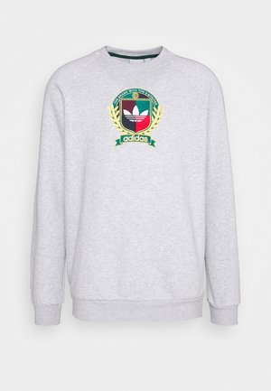 Sudadera gris claro con un emblema colorido de Adidas que presenta un escudo, hojas de laurel y el texto "THE BRAND WITH THE 3 STRIPES" en el pecho.