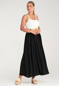 Weißes geripptes Tanktop, schwarzer plissierter Maxirock, breiter gewebter Gürtel mit runder Schnalle und Espadrilles mit Plateau.