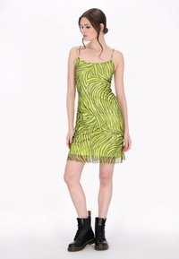 Rochie verde cu imprimeu zebra, cu bretele ajustabile, design aderent, material transparent și margine cu volane, asortată cu bocanci negri de luptă.