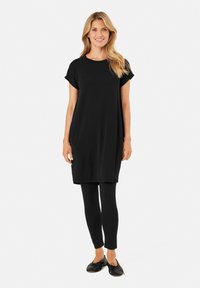 Robe tunique noire à manches courtes, assortie à des leggings noirs. Texture lisse, coupe décontractée, longueur genoux, design minimaliste et sans motifs.