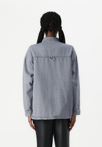 Giacca in denim grigio dal taglio rilassato, con colletto abbottonato e un dettaglio a ciclo sul retro. Maniche lunghe e polsini elastici.
