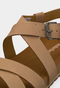 Πέδιλο από μπεζ δέρμα με σταυρωτούς ιμάντες και ασημένια πόρπη με χαραγμένο το "Timberland".