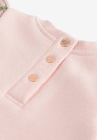 Rosa Sweatshirt mit Rundhalsausschnitt, der auf der Rückseite drei roségoldene Metallknöpfe und einen strukturierten Stoff aufweist.