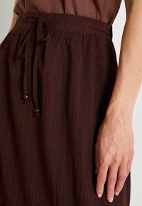Falda burdeos con un diseño texturizado y plisado, que cuenta con una cintura con cordón y dos botones decorativos en la línea de la cintura.