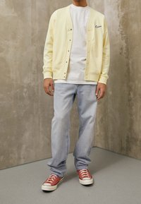 Light yellow cardigan with buttons, layered over a white t-shirt. Worn with light blue jeans and red sneakers with white soles.
