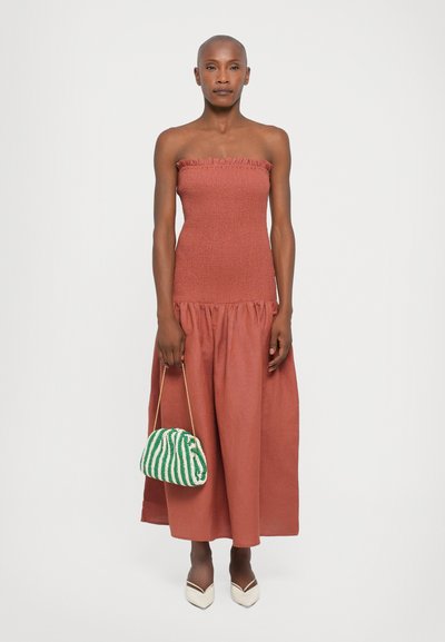 Robe rouge sans manches avec un corsage texturé et une jupe fluide, complétée par un sac rayé vert et blanc et des talons pointus couleur crème.