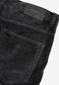 Sorte corduroy bukser med ribbet tekstur, en baglomme og et lædermærke med teksten "DENIM SUPPLY Co."