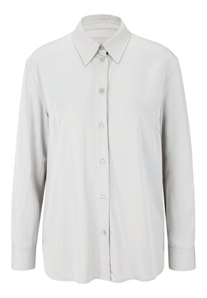 Chemise blanche à manches longues, unie, avec un col pointu et des poignets boutonnés, présentée sur un fond uni.