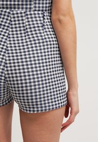 Pantalones cortos de cuadro vichy en azul marino y blanco, con bolsillos laterales, un diseño ajustado y una textura de tela suave.