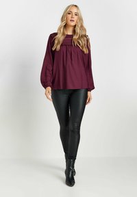 Maglietta bordeaux a maniche lunghe con scollatura arricciata e dettagli testurizzati, abbinata a pantaloni skinny neri effetto pelle e stivaletti.
