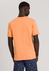 T-shirt arancione in cotone a maniche corte con scollatura rotonda, abbinato a pantaloni corti blu navy con un motivo di cerchi e spirali.
