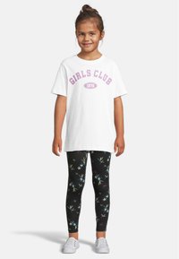 Hvit t-skjorte med teksten "GIRLS CLUB 1976" i lilla; parret med svarte leggings med flerfargede blomster-mønstre; hvite sko.