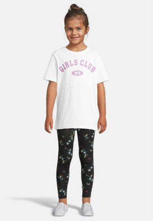 Hvit t-skjorte med teksten "GIRLS CLUB 1976" i lilla; parret med svarte leggings med flerfargede blomster-mønstre; hvite sko.