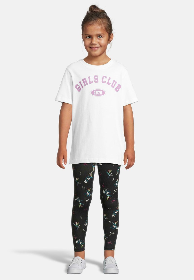 Hvit t-skjorte med teksten "GIRLS CLUB 1976" i lilla; parret med svarte leggings med flerfargede blomster-mønstre; hvite sko.