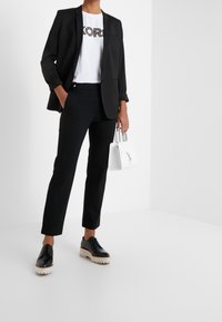 Czarna marynarka na białym t-shircie z grafiką i napisem "KORS", w połączeniu z czarnymi spodniami o dopasowanym kroju oraz czarnymi skórzanymi butami na grubej podeszwie. Biała torebka.