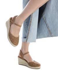Sandali wedge perforati marrone con cinturino alla caviglia, suola avvolta in juta e tomaia texturizzata, abbinati a pantaloni cropped in denim chiaro.