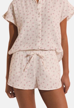 Miękka różowa koszula z krótkim rękawem na guziki oraz dopasowane szorty ze ściągaczem i małym różowym kwiatowym wzorem na modelce.