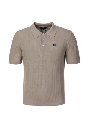Beige kortærmet strikket poloshirt med tre hvide knapper og et lille mørkt broderet logo på venstre bryst.
