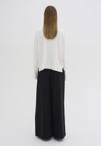 Biały sweter z dzianiny o luźnym kroju, zestawiony z czarnymi spodniami o szerokich nogawkach. Sweter ma opadające ramiona i boczne rozcięcia.