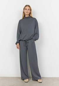 Grijs loungewear-set met hoge hals, lange mouwen en elastische tailleband. Brede pijpen met een trekkoord, gemaakt van zacht materiaal.
