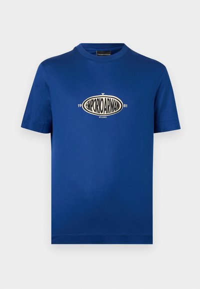Μπλε κοντομάνικο T-shirt με στρογγυλή λαιμόκοψη, με οβάλ λογότυπο Emporio Armani σε εκρού και μαύρο, που βρίσκεται στο κέντρο του στήθους, με τα κείμενα "1981" και "Milano".