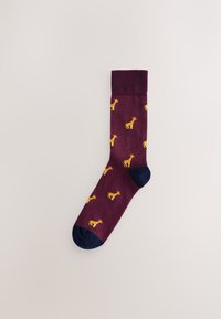 Chaussette bordeaux ornée d'un motif de petites girafes jaunes, talon et bout foncés en bleu marine, bord-côte côtelé et texture lisse.