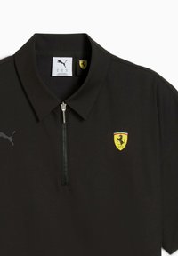 Sort polo shirt med lynlås krave, Puma-logo på venstre ærme og Ferrari-våbenskjold på fronten.