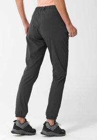 Pantalones jogger ligeros grises con cinturilla elástica, puños ajustados y textura suave. Llevados con zapatillas negras que tienen acentos grises.