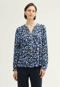 Bluzka z długim rękawem w ciemnoniebieskim kolorze z kwiatowym wzorem w różnych odcieniach niebieskiego i zielonego. Posiada dekolt w kształcie litery V oraz detal z guzikami.