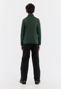 Camicia verde a maniche lunghe con colletto alto, vestibilità slim e texture liscia, abbinata a pantaloni neri e scarpe nere robuste.
