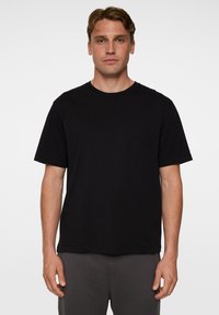 Mustat, lyhythihainen t-paita pehmeästä kankaasta, jossa on pyöreä kaula-aukko ja rento istuvuus. Ei näkyviä logoja tai kuvioita.