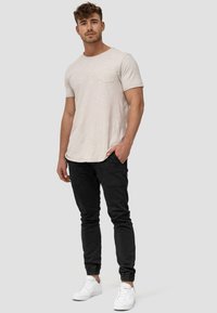 Camiseta beige de manga corta con un bolsillo, combinada con pantalones tipo jogger negros con puños elásticos y zapatillas blancas.