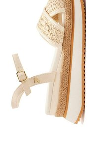 Sandale compensée tressée beige avec une sangle de cheville réglable, semelle blanche et détails en jute texturé le long de la plateforme. Accents en métal doré.