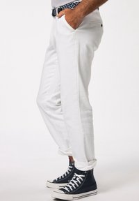 Pantaloni bianchi in cotone con una vestibilità rilassata, dotati di tasche laterali e orli arrotolati. Abbinati a sneakers alte blu navy.