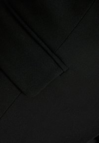 Černá tkanina s texturovaným povrchem, se skládáním na okraji a jemnými detaily šití. Čisté linie bez viditelného kovového nářadí nebo vzorů.