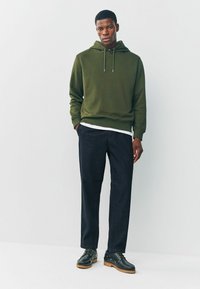 Olive green hoodie with drawstrings, paired with dark pants and black shoes. Smooth texture, relaxed fit, casual design.