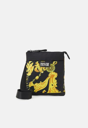 Petit sac bandoulière noir avec motif baroque doré et étiquette Versace Jeans Couture sur la poche avant, fermeture éclair sur le dessus.