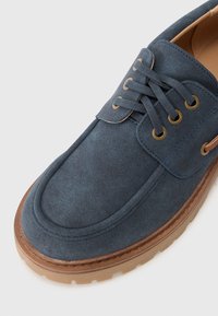 Herrenblaue Wildlederschuhe mit runder Zehenform, Schnürdesign, goldfarbenen Ösen und einer kontrastierenden braunen Gummisohle.