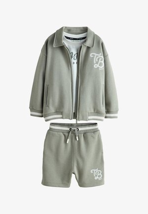 Matchende lichtgrijze zip-up jas en short set met witte gestreepte boorden, trekkoord in de taille en wit "TB Baker" logo op beide delen.