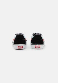 Svart-hvite joggesko med røde og akvamarin aksenter; laget av skinn og lerret; har en hvit såle og Vans-logo på hælen.