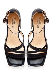 Zwarte hoge hakken sandalen met een vierkante neus, voorzien van kruislings banden en een enkelgesp. Gladleren textuur met een contrasterende beige binnenzool.