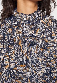 Blusa con scollatura arricciata e chiusura a bottoni, caratterizzata da un design a fantasia in blu navy, bianco e tonalità di arancione, realizzata in tessuto leggero.