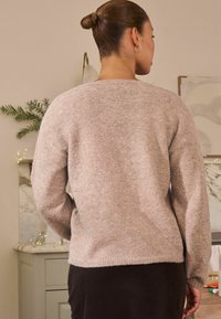 Lyse beige sweater med en blød tekstur, rund halsudskæring og lange ærmer. Bagsiden har en sømløs strik og en let buet kant.