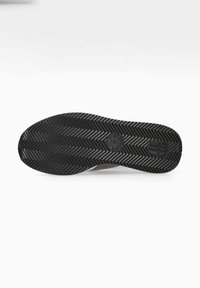 Semelle de chaussure en caoutchouc noir avec un motif en chevrons, comportant un logo et des rainures pour la traction ; le bord supérieur présente une accentuation marron clair.