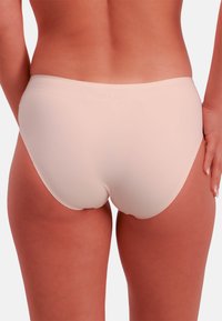 Bas de bikini couleur pêche, sans coutures, avec une texture lisse, une couvrance modérée et une taille mi-haute, conçu pour le confort et la flexibilité.